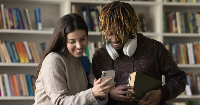 Two students smiling while looking at a phone
